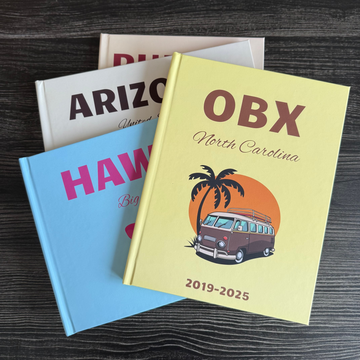 Three travel photobooks with different designs on a wooden surface