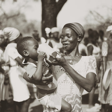 Black and white photograph of a woman holding a child in a crowded outdoor setting.