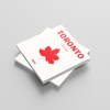 Stack of square photobooks with a red maple leaf and 'Toronto' text on a gray background