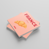 Two pink square photobooks with a croissant illustration and 'France' text on a gray background