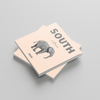 Two square photobooks stacked on a light gray background, with one book showing an elephant illustration and displaying text of 'South Africa'