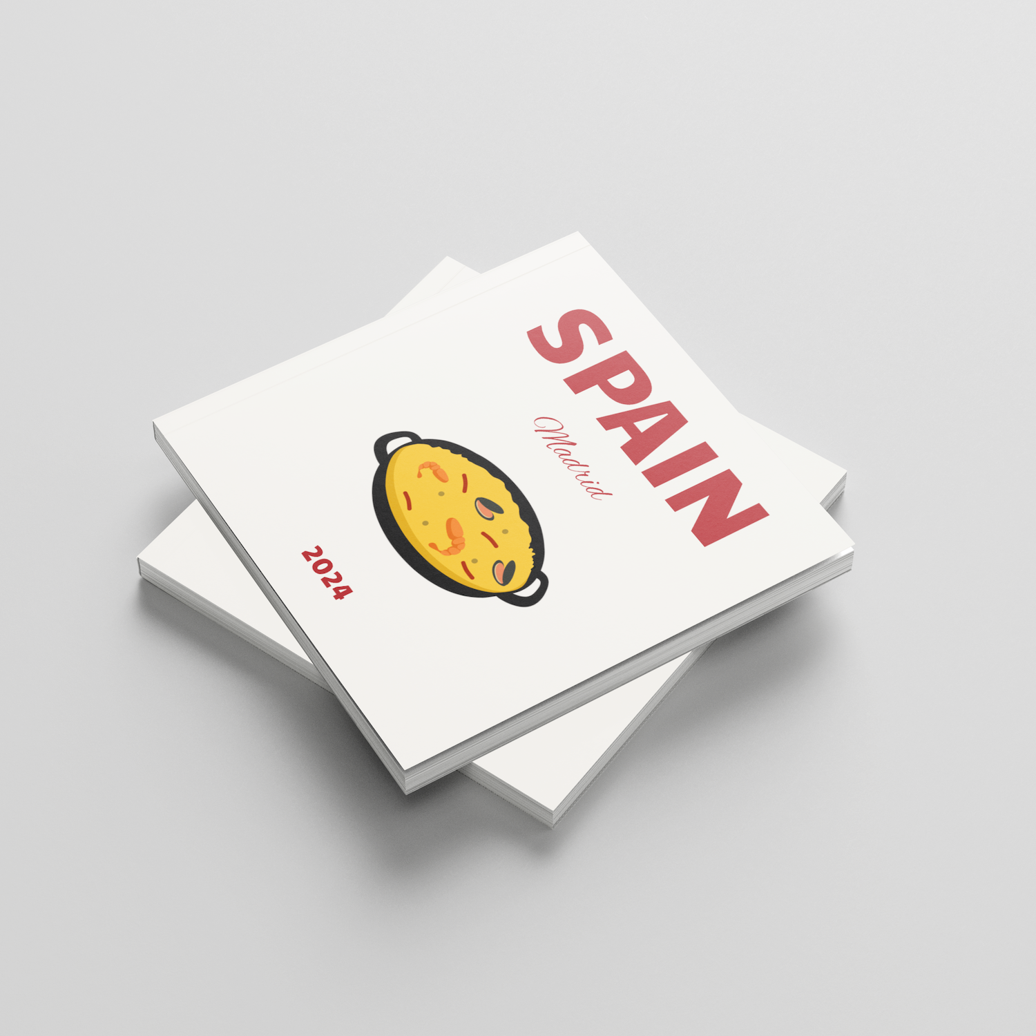 Stack of white square photobooks with a colorful illustration and 'SPAIN' text on a light gray background